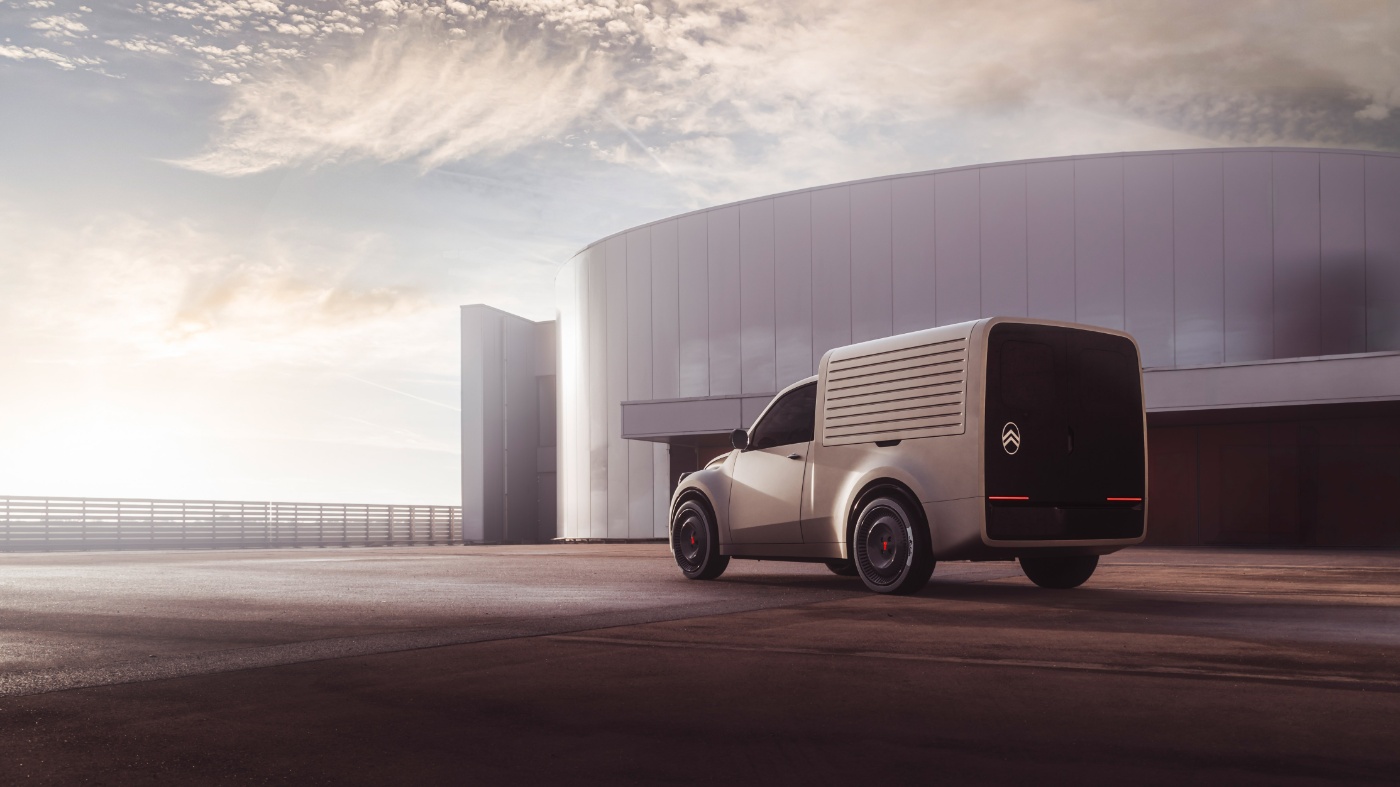 White Citroën delivery van viewed from behind, parked in front of a large modern building at sunset.