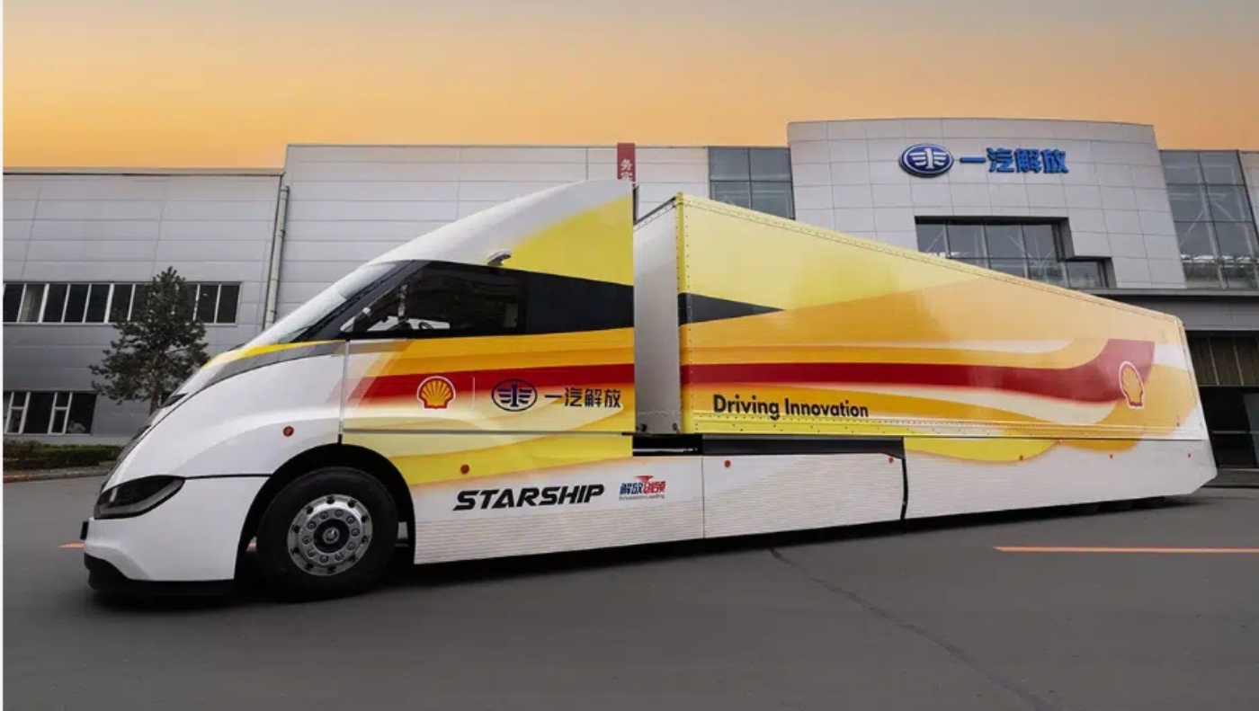White STARSHIP bus with red and yellow stripes parked in front of an industrial building at sunset.