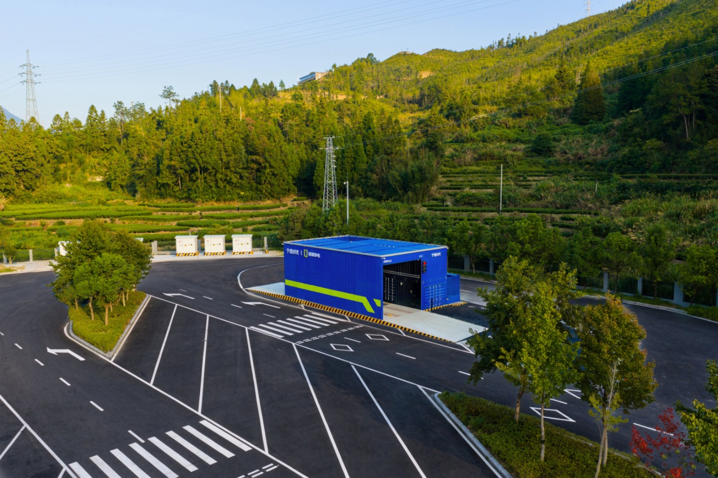 Teststrecke mit Fahrbahnmarkierungen und blauem Gebäude, umgeben von Bäumen und bewaldeten Hügeln.
